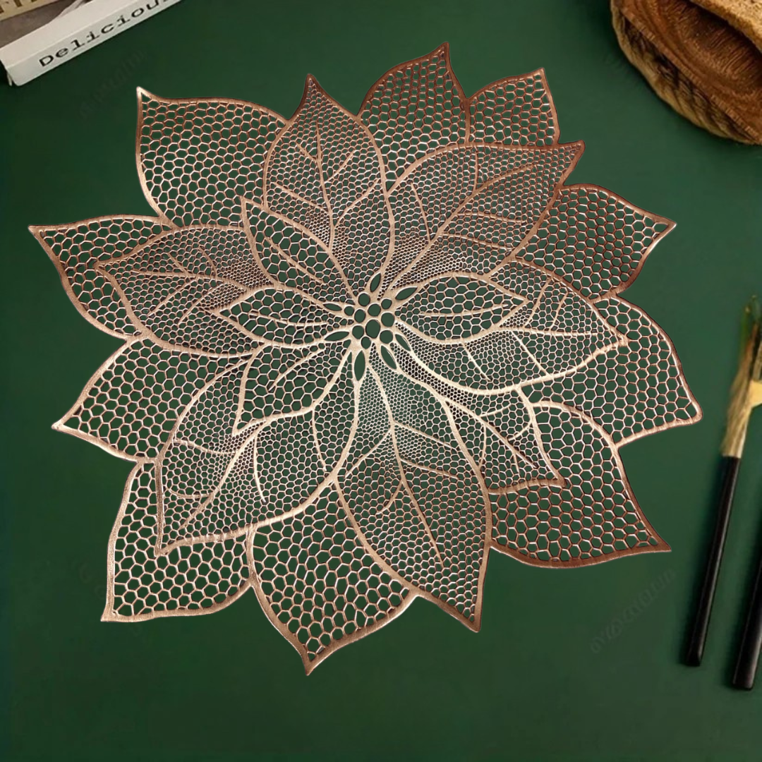 White bowl and small dish with spoon on a lace-like, leaf-shaped Copper table mat over a green surface.