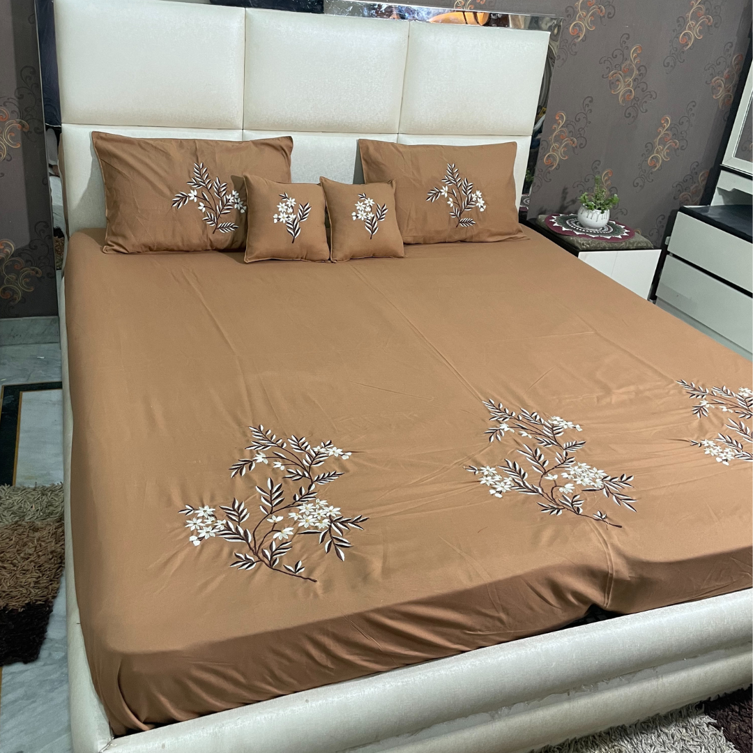 Brown color glace  cotton bedsheet set of 5 embroidered with floral design 2 cushion covers and 2 pillow covers placed on a bedsheet