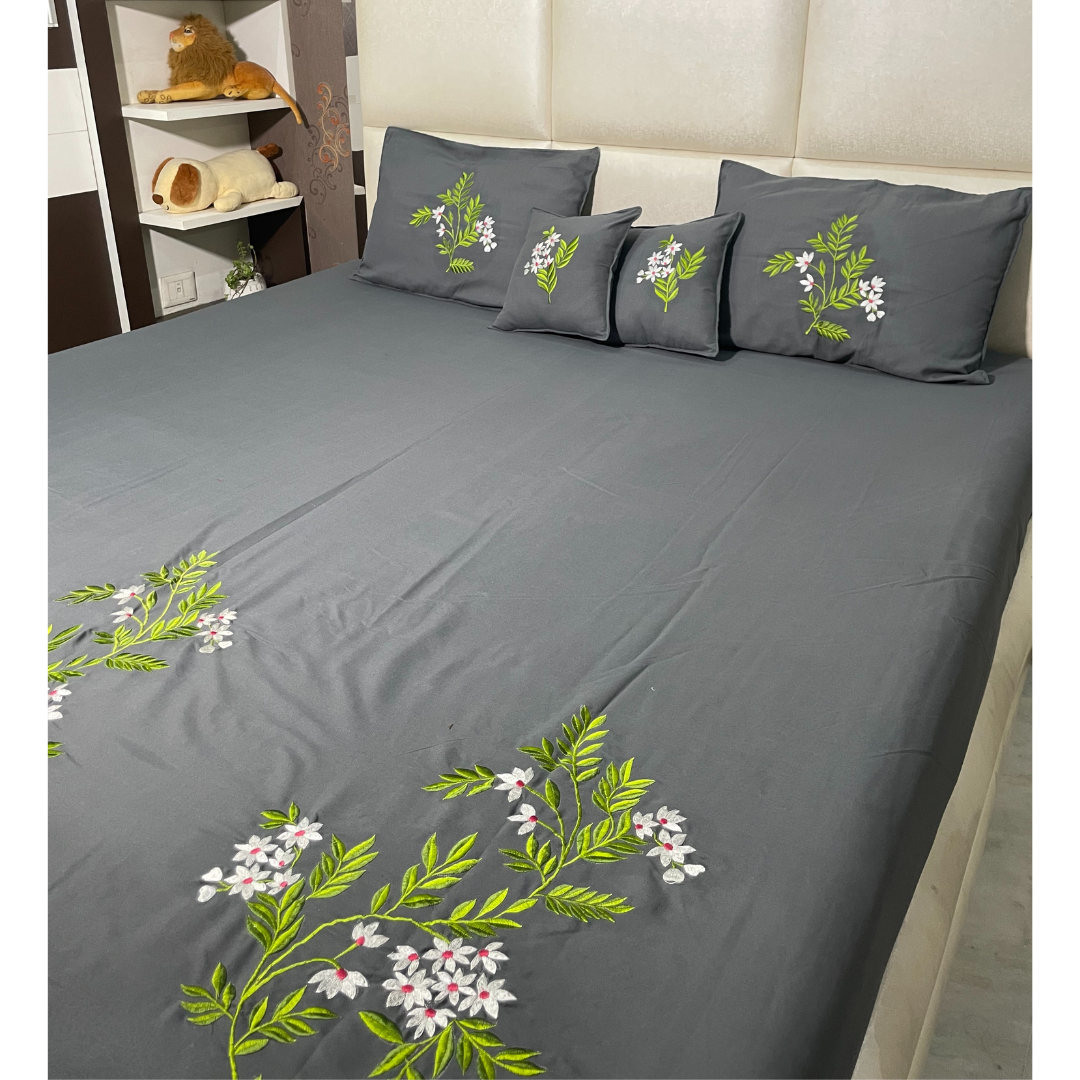 Grey color glace cotton bedsheet set of 5 embroidered with floral design 2 cushion covers and 2 pillow covers placed on a bedsheet