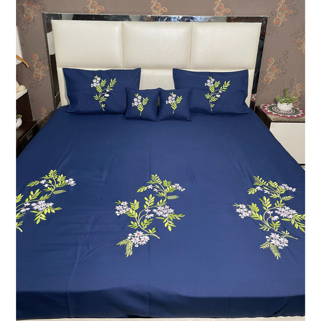 Blue color glace  cotton bedsheet set of 5 embroidered with floral design 2 cushion covers and 2 pillow covers placed on a bedsheet