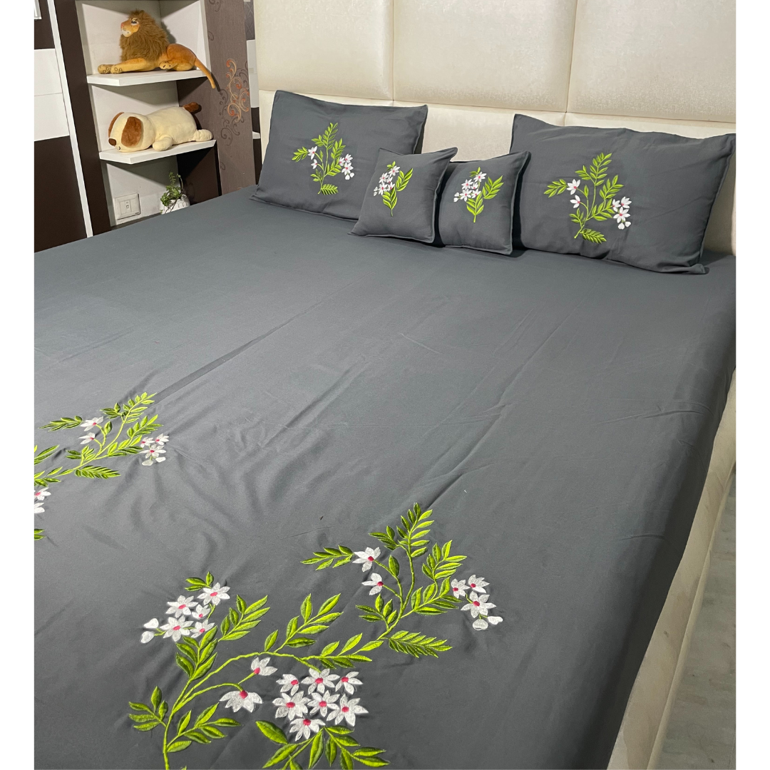 Grey color glace  cotton bedsheet set of 5 embroidered with floral design 2 cushion covers and 2 pillow covers placed on a bedsheet