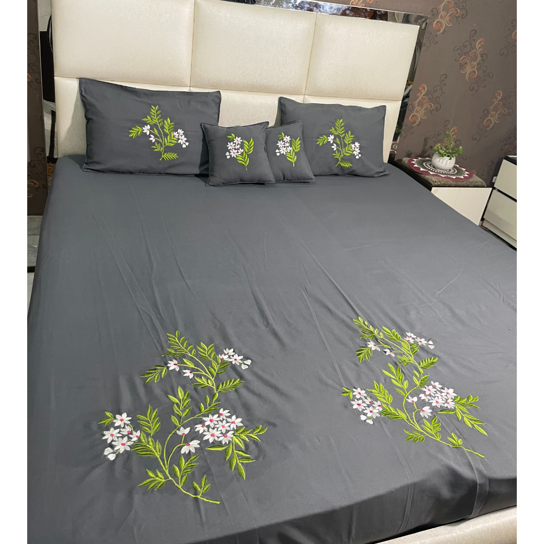 Grey color glace  cotton bedsheet set of 5 embroidered with floral design 2 cushion covers and 2 pillow covers placed on a bedsheet