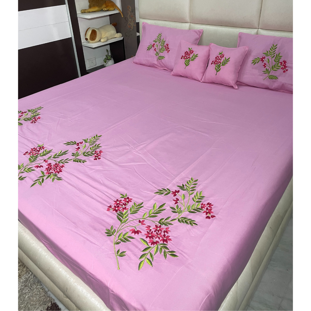 Pink color glace  cotton bedsheet set of 5 embroidered with floral design 2 cushion covers and 2 pillow covers placed on a bedsheet