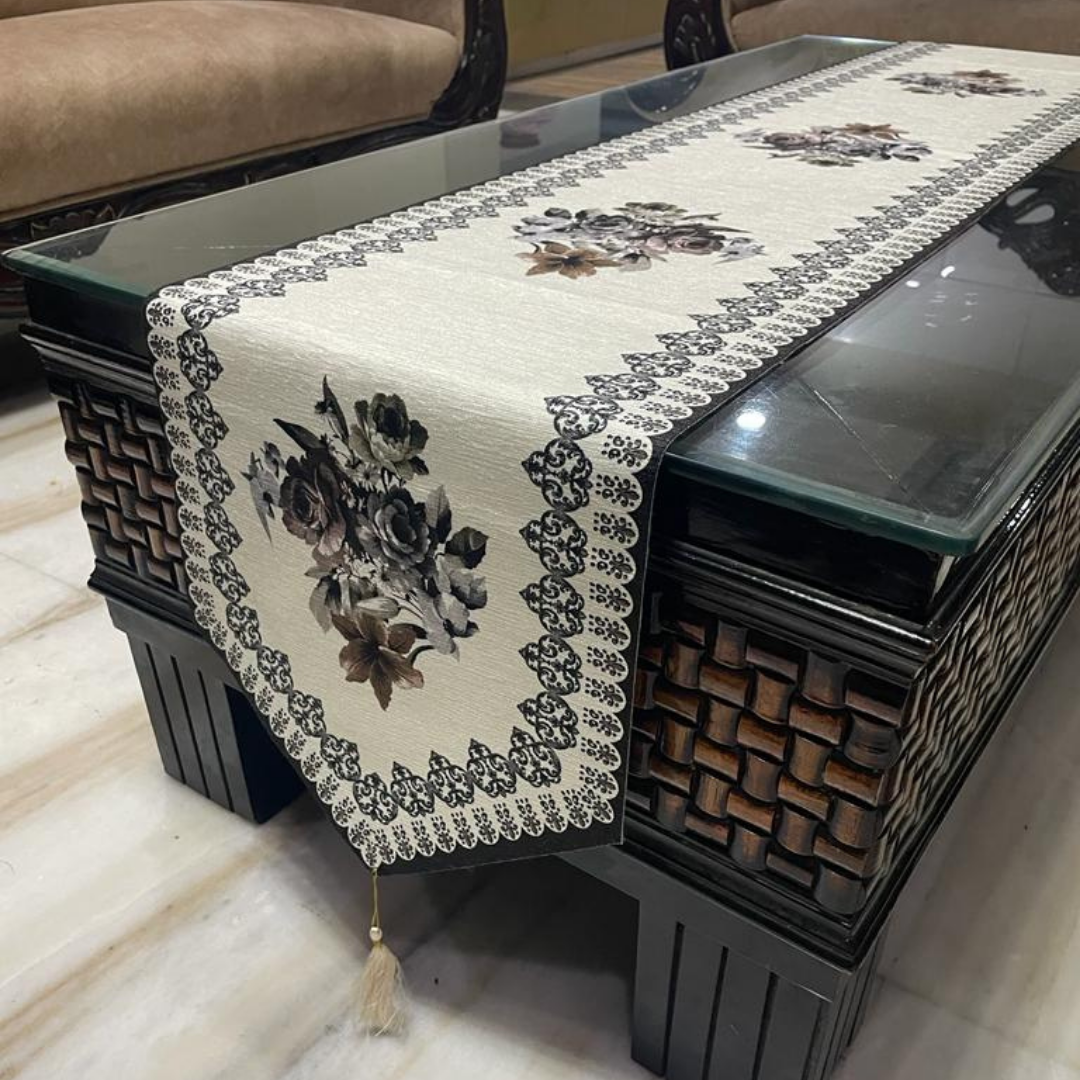 floral printed dining table runner in grey color design with a tassel on both ends borders printed placed on glass wooden table Side view