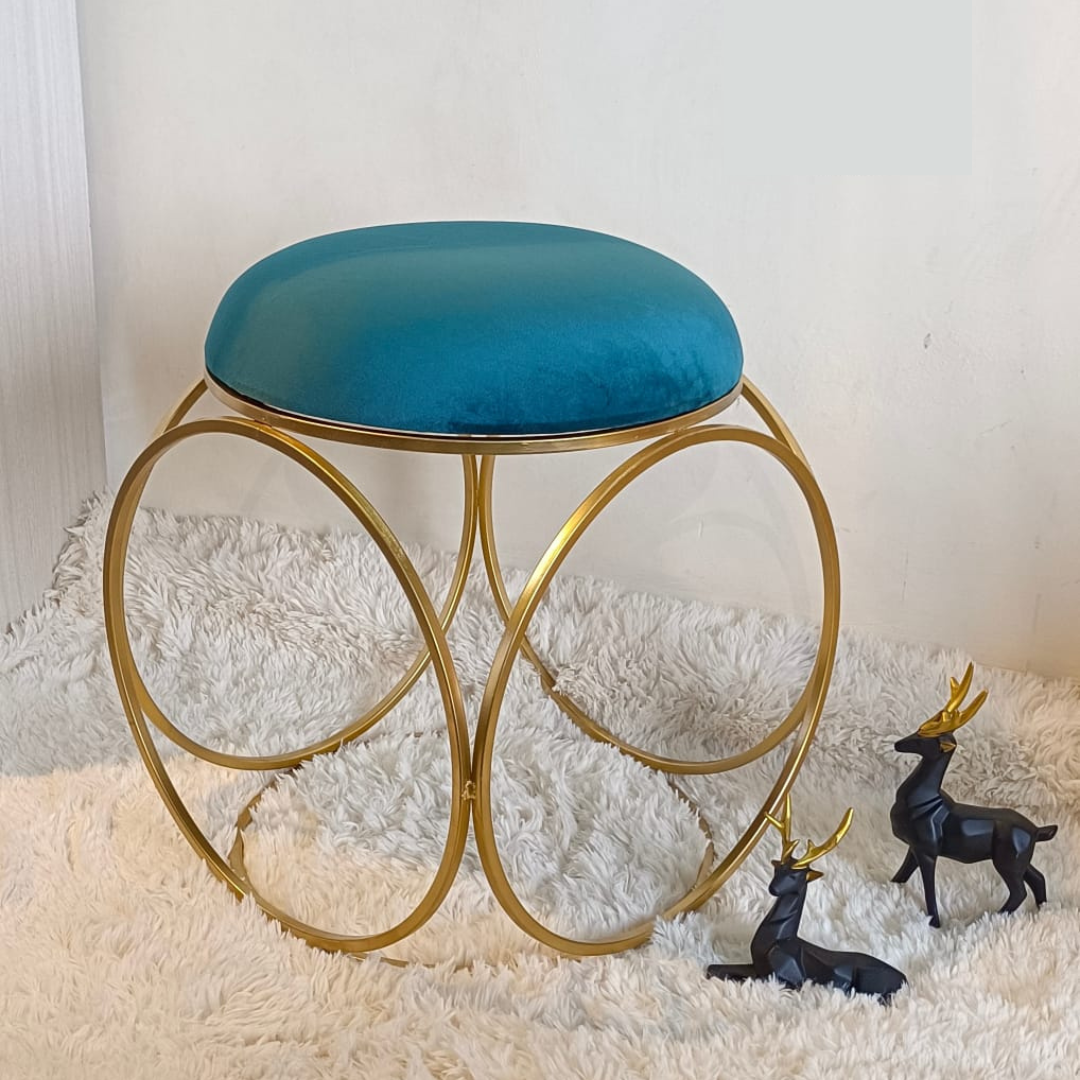 round design gold metal stool with puffy top in blue color placed on soft rug