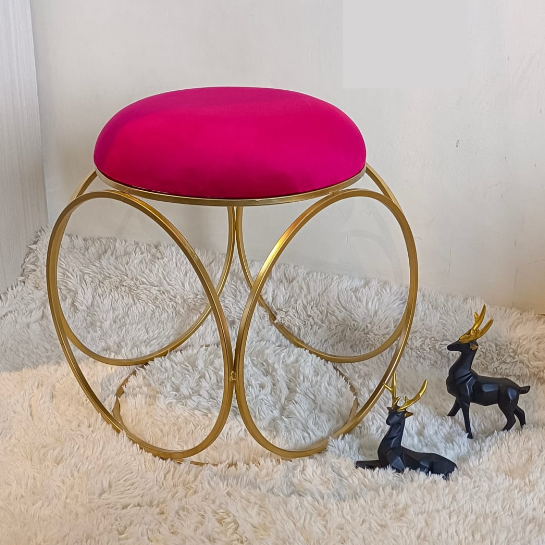 round design gold metal stool with puffy top in pink color placed on soft rug
