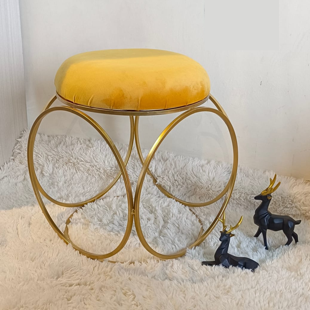 round design gold metal stool with puffy top in yellow color placed on soft rug