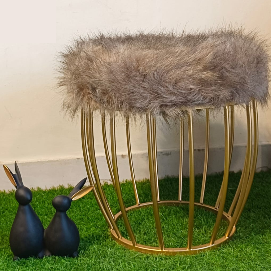 metal stool gold color placed on faux grass mat with brown fur top rabbit showpiece placed near ottoman