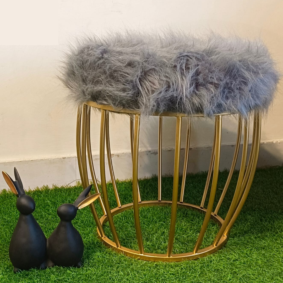 metal stool gold color placed on faux grass mat with Grey fur top rabbit showpiece placed near ottoman