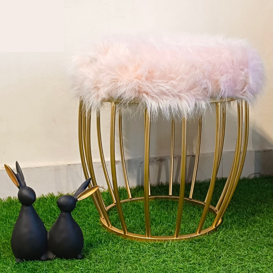 metal stool gold color placed on faux grass mat with pink fur top rabbit showpiece placed near ottoman