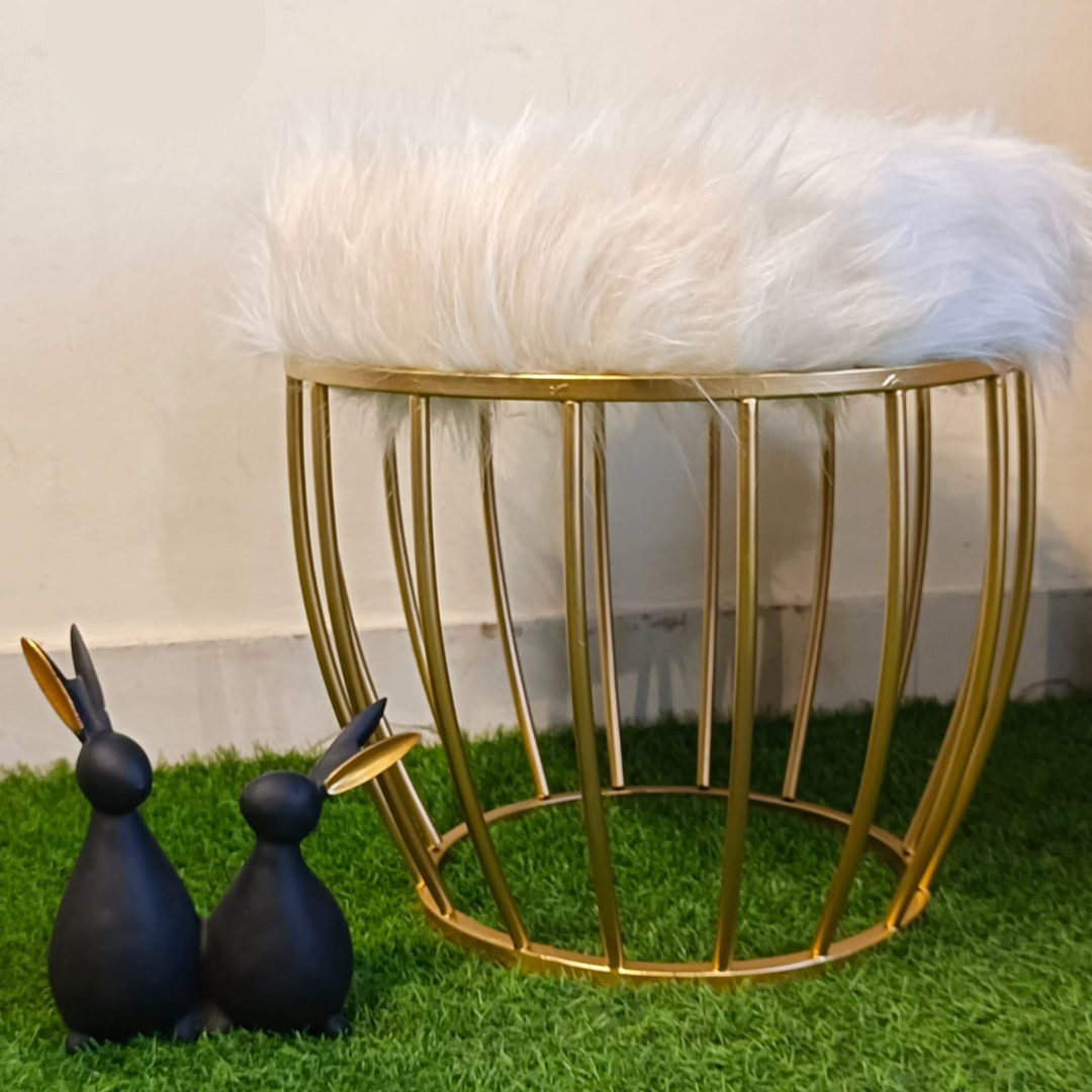 metal stool gold color placed on faux grass mat with white fur top rabbit showpiece placed near ottoman