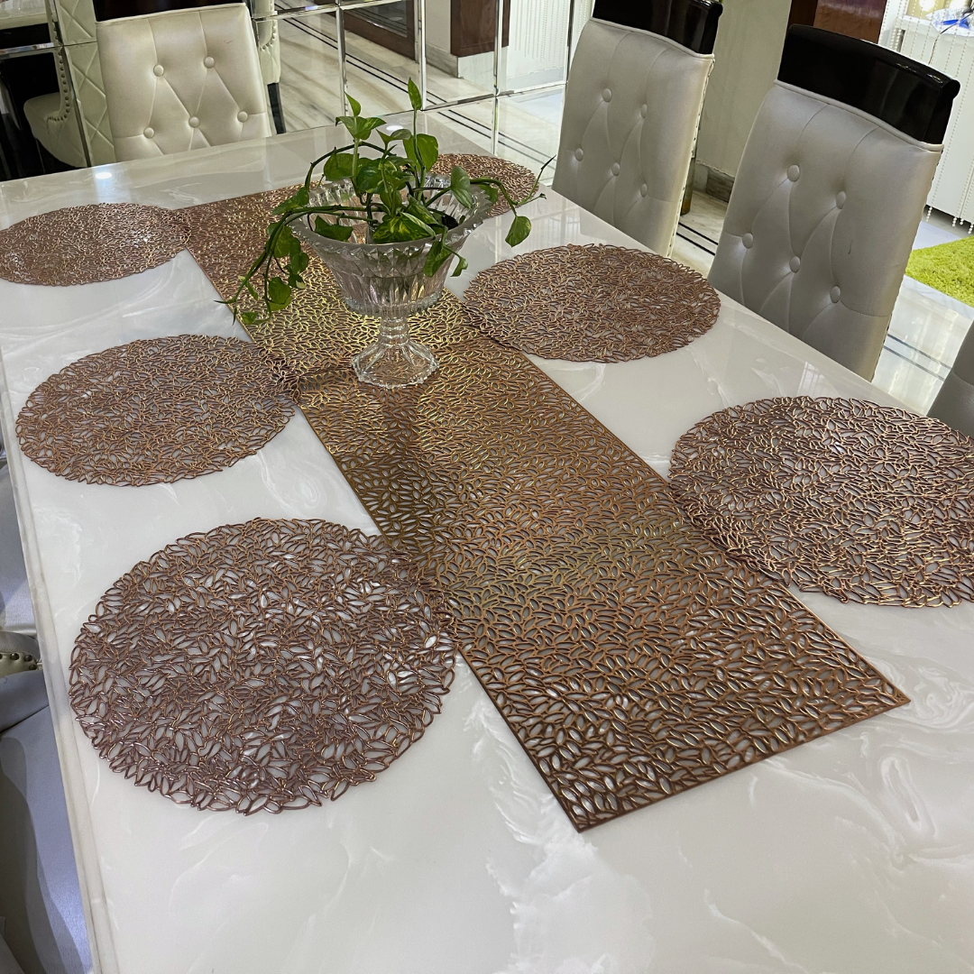 metallic look round placemats in copper color with long runner placed on white marble table accessorized with glass pot
