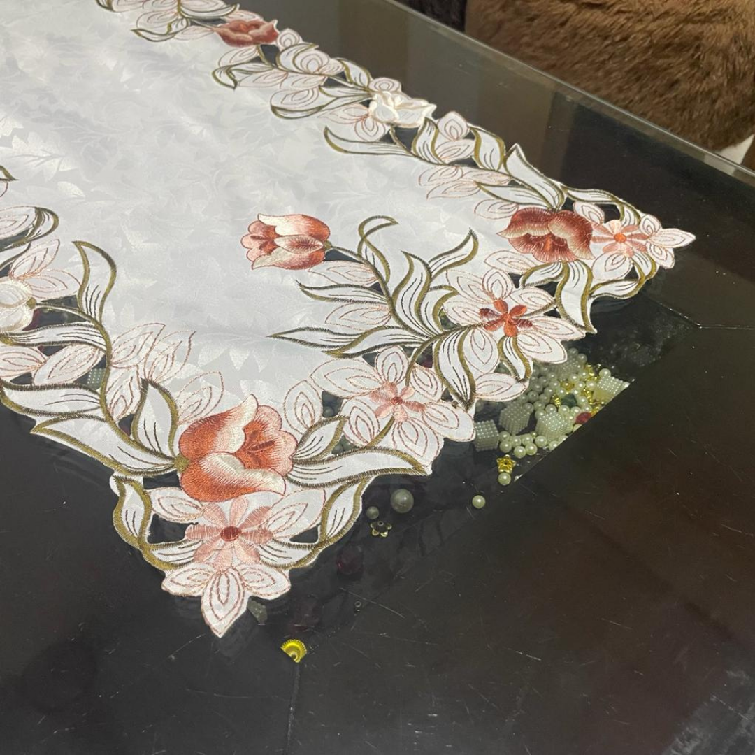 Brown flower and green leaves embroidery on center table runner of tissue fabric placed on black glass center table