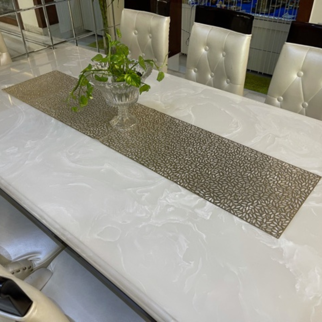 metallic look dining table runner in gold color placed on white marble dining table set of 6 glass pot placed on it