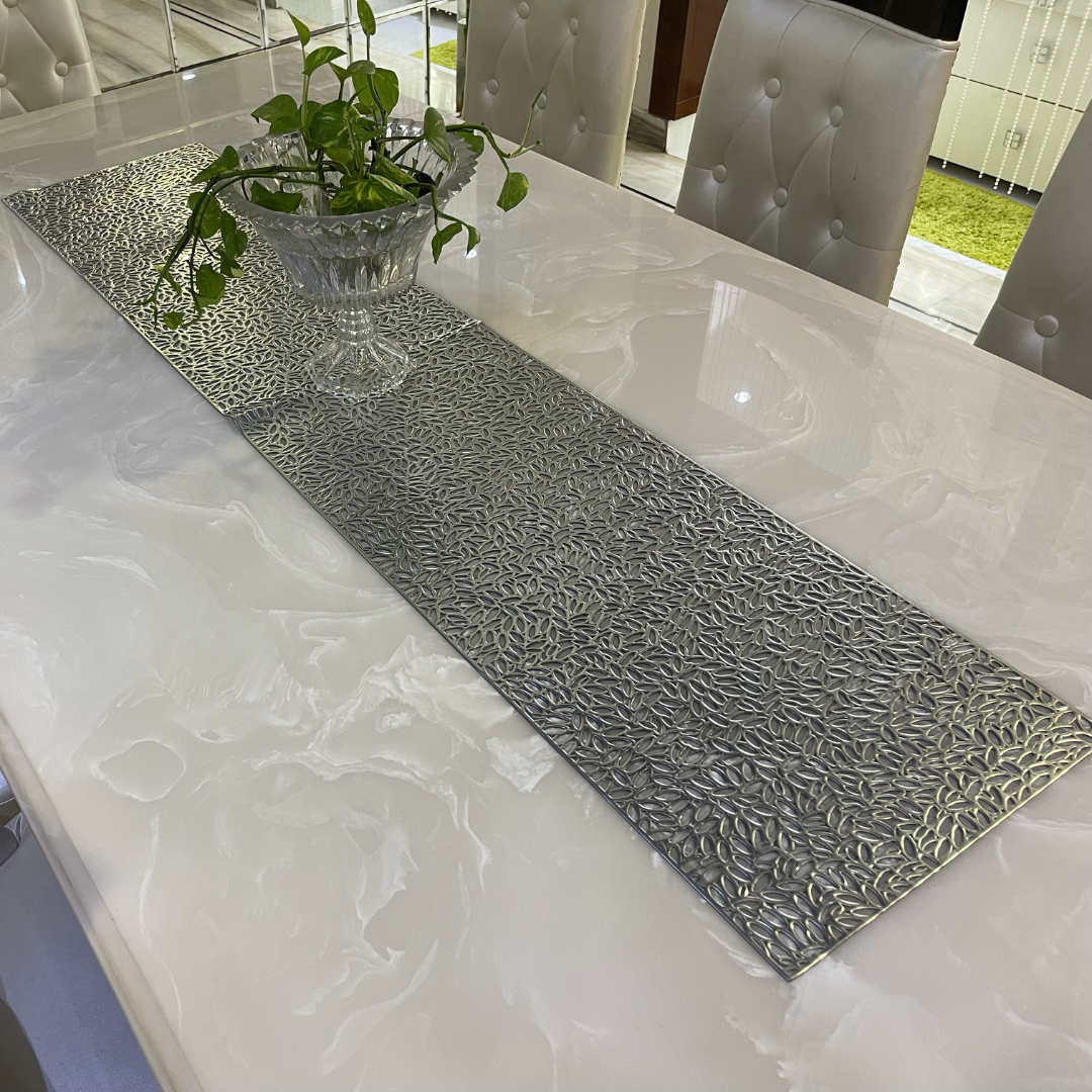 metallic look dining table runner in silver color placed on white marble dining table set of 6 glass pot placed on it