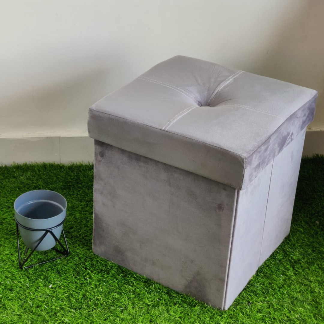 solid grey color velvet storage box with stool foam sitting small pot placed near stool on faux grass floor