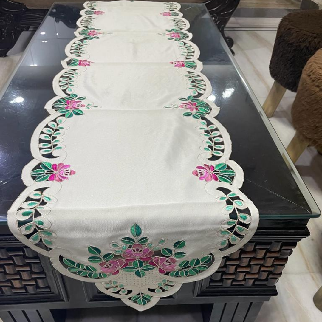 tissue fabric table runner embroidered with pink flowers and green leaves on border shaped cut design placed on the dining table front view