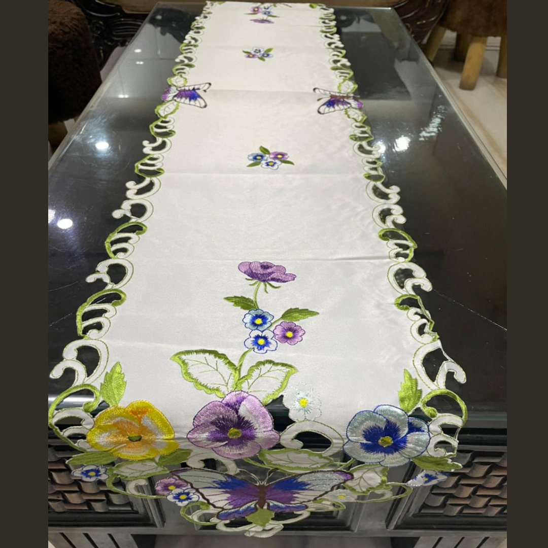 tissue fabric table runner embroidered with purple blue flowers and green leaves on border shaped cut design placed on the dining table front view